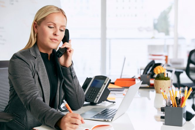 A woman using the telephone at her desk.