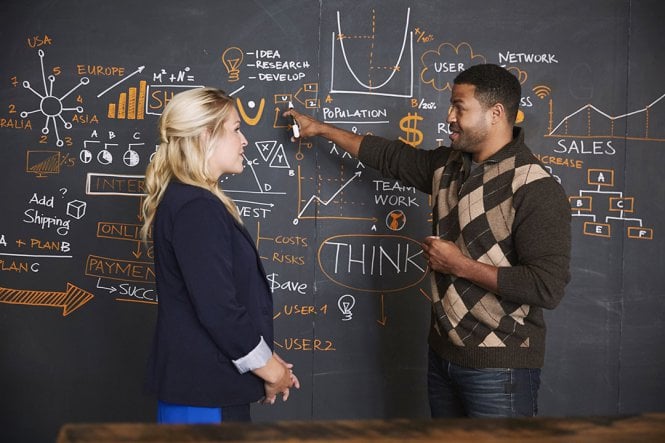 A man and a woman in front of a blackboard with equations on it.