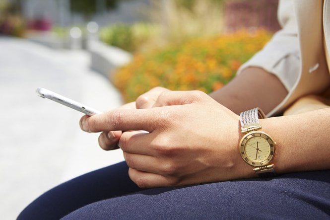 Man wearing watch sits and uses smartphone.