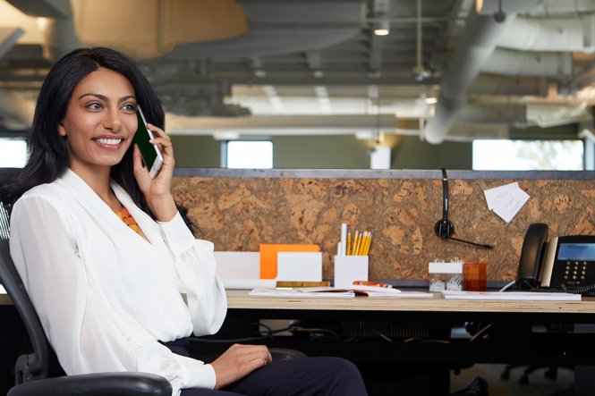 A woman sitting at her desk, speaking on her mobile phone.