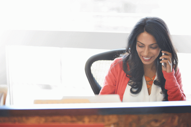 A woman sitting at a desk, talking on her mobile phone.