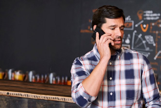 A man standing in front of a blackboard, talking on a mobile phone.