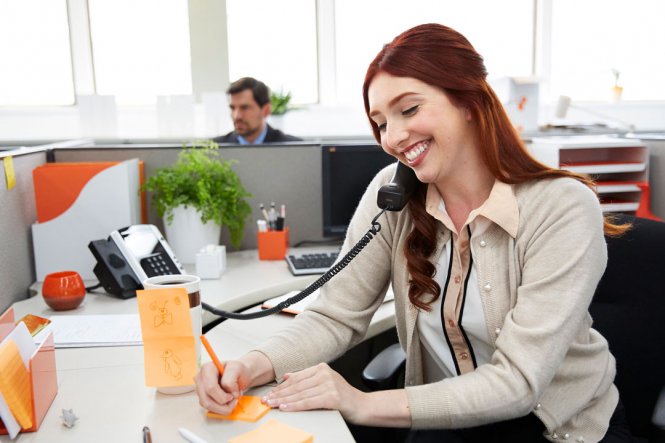 A smiling woman talking on an office telephone.