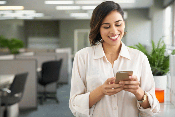 A smiling woman in an office, using a mobile phone.