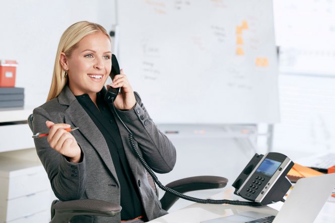 A woman sitting at a desk, talking on an office phone.
