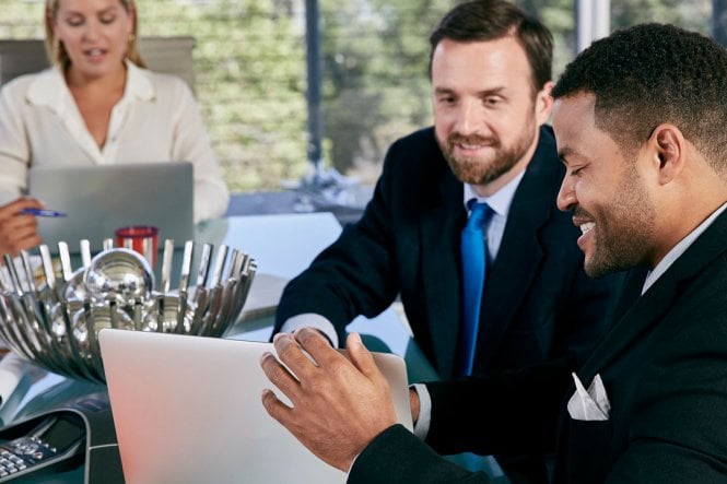 Two men and a woman in a conference room, viewing laptops.