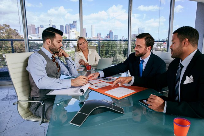 Three men and a woman in an office, reviewing a contract.