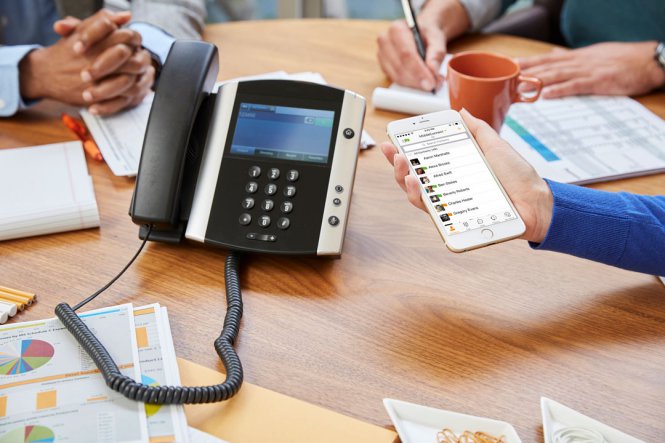 Colleagues working at a table, with an office phone and a smartphone.