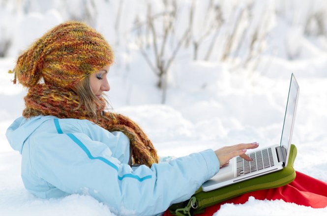 Young woman outside in snow using laptop.