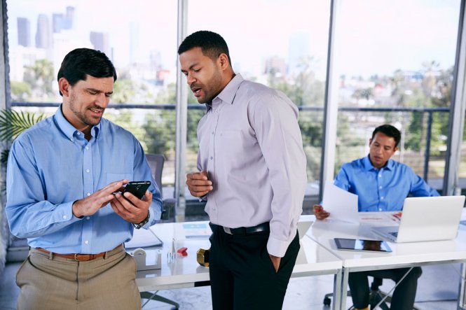 Two men talking in an office, with one of them using a smartphone.
