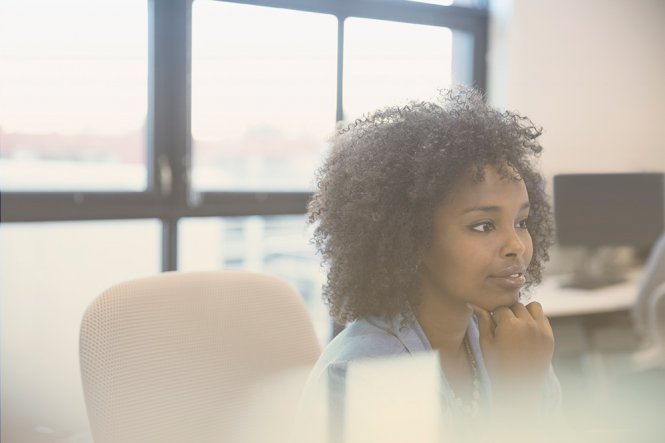 A woman sitting in an office, listening intently to someone speaking.