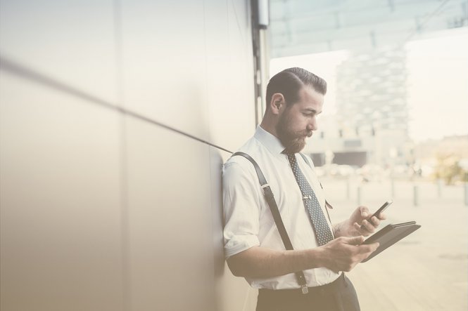 A man standing outside, using a tablet and a mobile phone.
