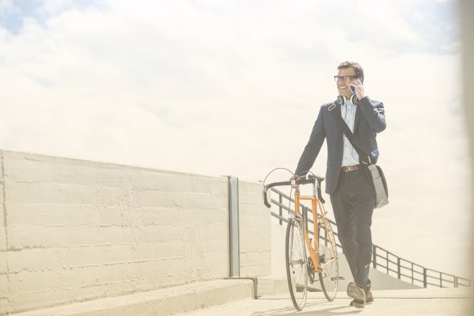 A man walking his bike while talking on a mobile phone.