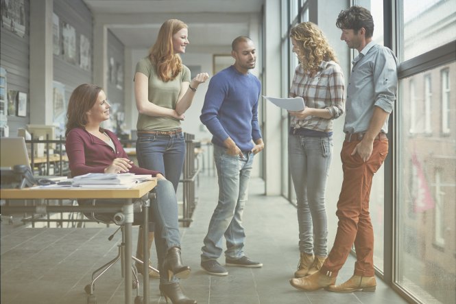 Two men and three women meeting in a casual office environment.