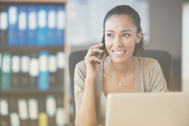 A woman talking on the phone while sitting at a computer in her office.