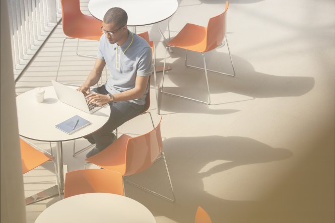 A man sitting outside at a table, using his laptop.