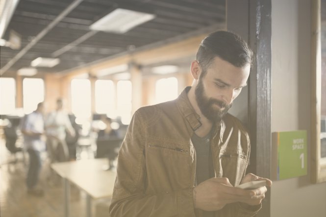 A man using his smartphone in an open, modern office building.