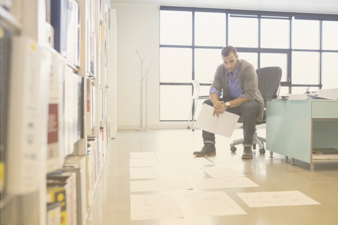 A man reviewing documents, which are laid out on his office floor.