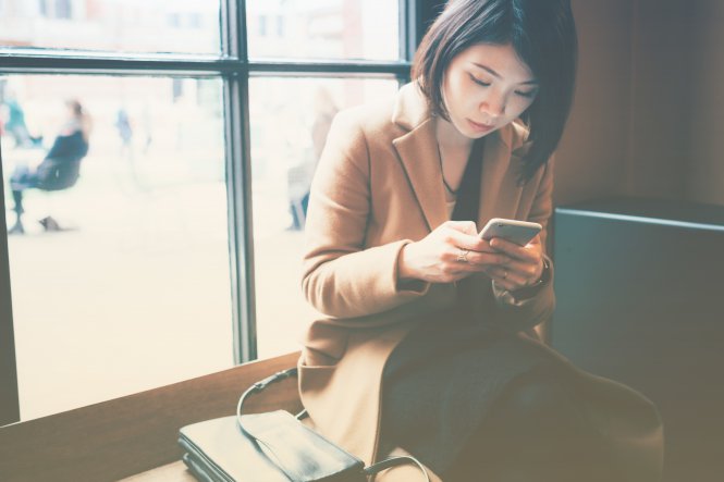 A woman sitting by a window, using her smartphone.