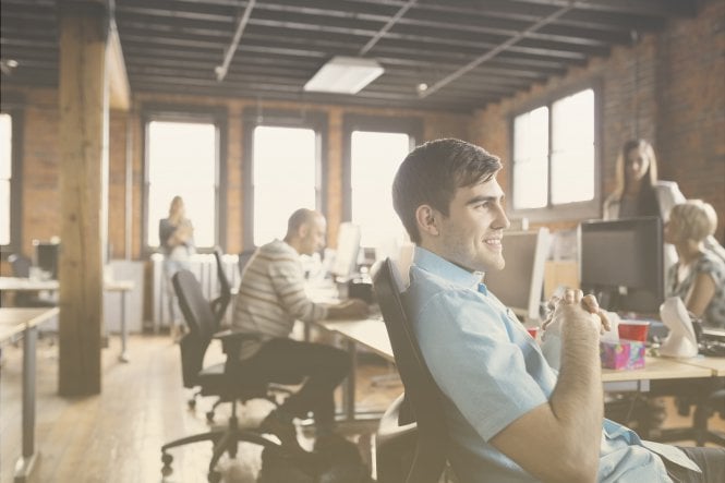 A smiling man sitting back at his desk in an open, modern office.