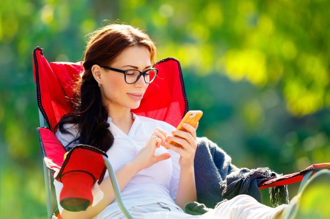 A woman using her smartphone from a lawn chair, highlighting one of the benefits of the cloud.