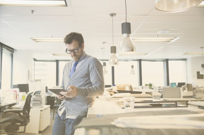 A man standing up by a desk, using a tablet.