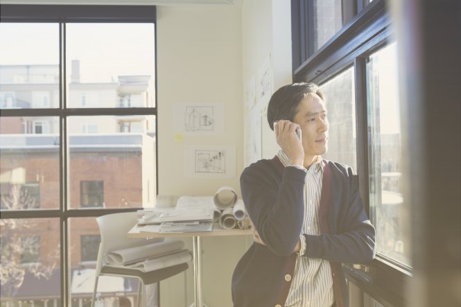 A man standing by his office window, talking on his smartphone.