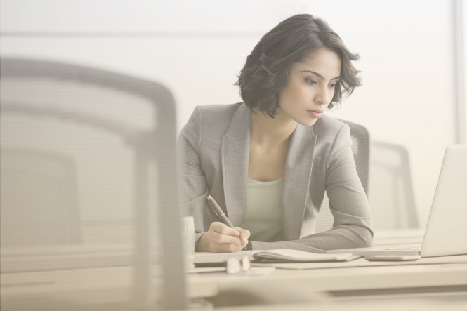 A woman taking notes at her desk, because she doesn't have cloud-based call recording.