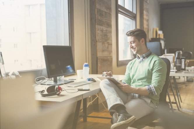 A man smiling at his desk because his manager uses virtual meeting technology to show appreciation.
