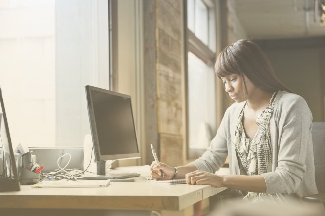 A woman writing at her desk, benefiting from new technology in business.