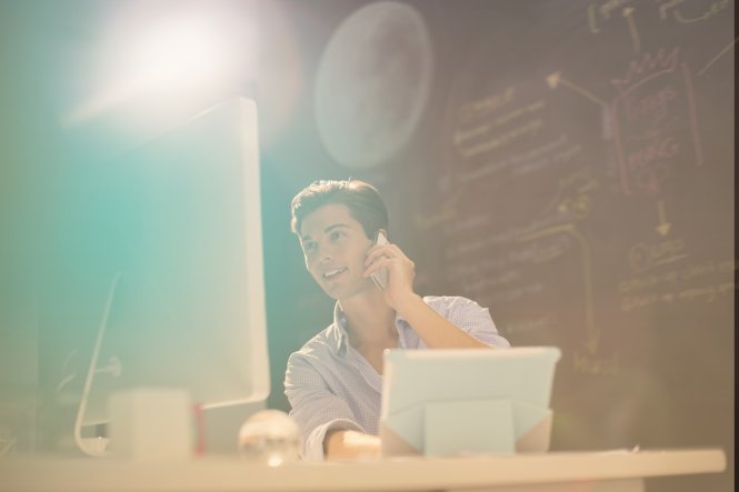 A man using a computer while talking on a smartphone, benefiting from communication in business.