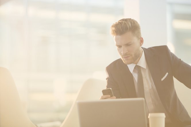 A man in a suit using a smartphone and a laptop.