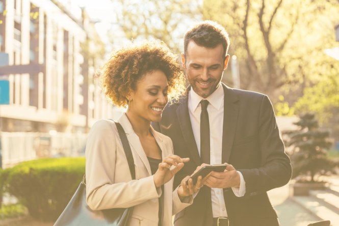 A businesswoman and businessman using their smartphones outside.