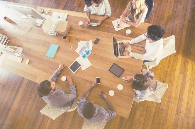 A team of coworkers sitting around a table, making a top-down decision on technology in business.