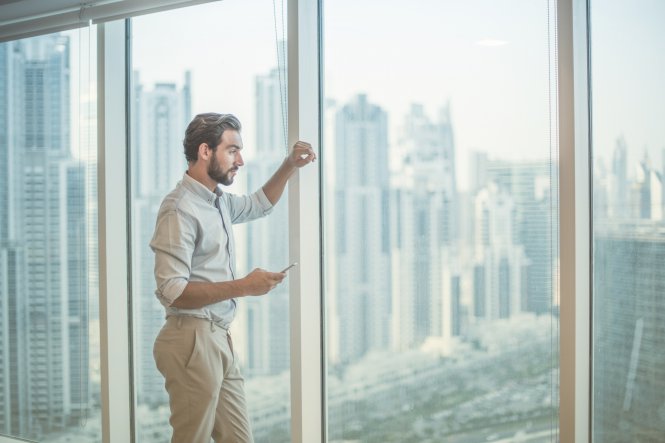 A man using LTE communication on his smartphone while looking out his office window.
