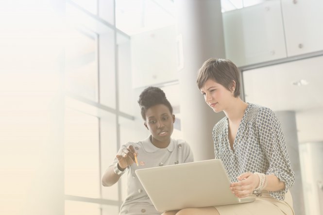 Two women viewing a laptop computer in an office, protected by HIPAA cloud compliance.