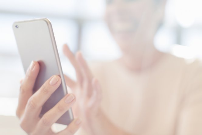 A smiling woman holds a mobile phone while engaging in doctor-patient communication