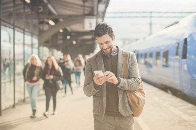 Man on a train platform receives a meeting reminder SMS on his phone