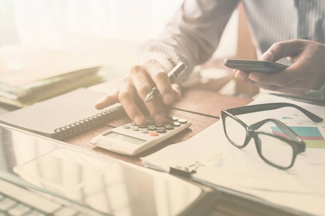 An accountant embracing disruption by using a smartphone alongside a calculator, charts and a laptop
