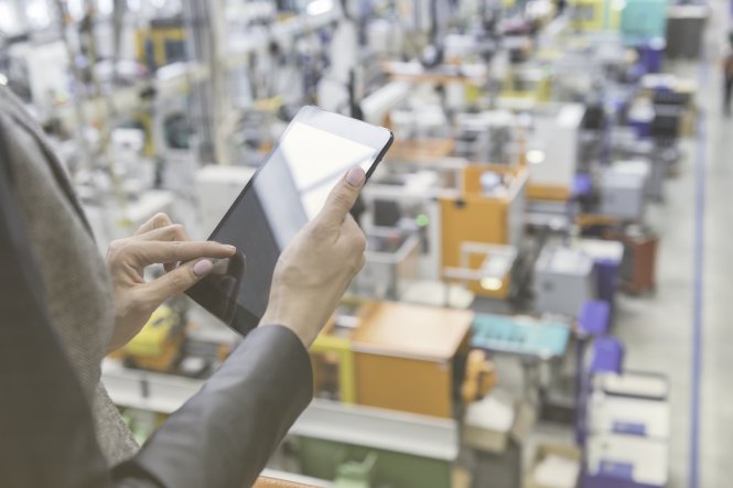 Person using tablet in front of a backdrop of manufacturing jobs and machinery