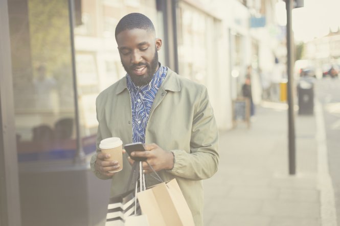 Person walking down street with shopping bags, phone, and coffee — requirements of enterprise CPaaS