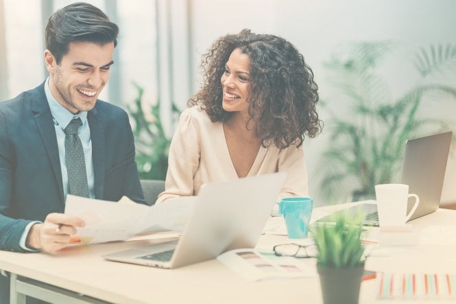 Two professionals laughing while looking at documents and a laptop — UCaaS applications