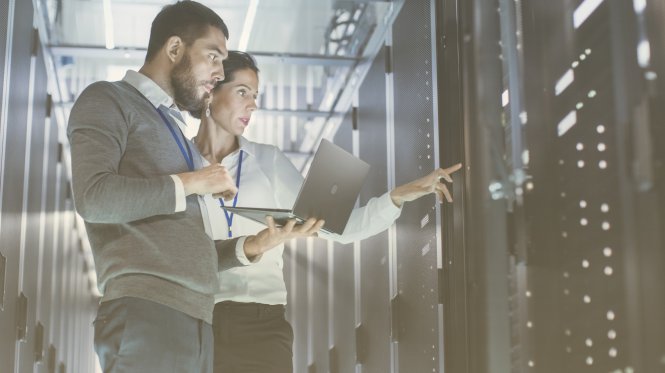 Two IT professionals holding a laptop and looking at servers — office safety communication tools