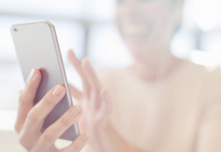 A smiling woman holds a mobile phone while engaging in doctor-patient communication