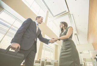 A businessman and woman shakes hands and discuss the challenges of recruitment and selection