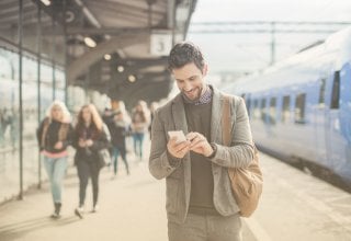 Man on a train platform receives a meeting reminder SMS on his phone
