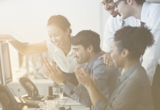 A group of employees enthusiastically engage with a desktop computer