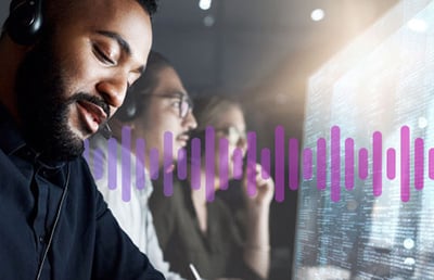 Man wearing a headset working in front of a computer screen displaying data, as a man and woman colleague work in the background
