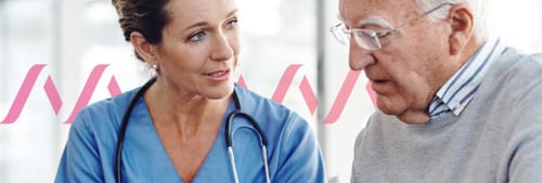 Photo of a female doctor in blue scrubs seated with a stethoscope draped across her neck and a tablet in her hand, which is she showing to an elderly white-haired man who is her patient
