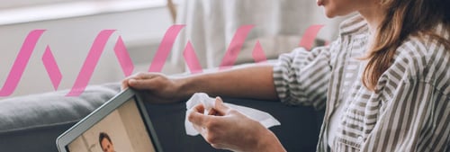 Image of woman, sitting with a laptop. She’s holding a tissue and conducting a virtual doctor’s visit.